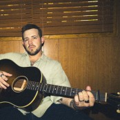 A man wearing a green shirt holding an acoustic guitar